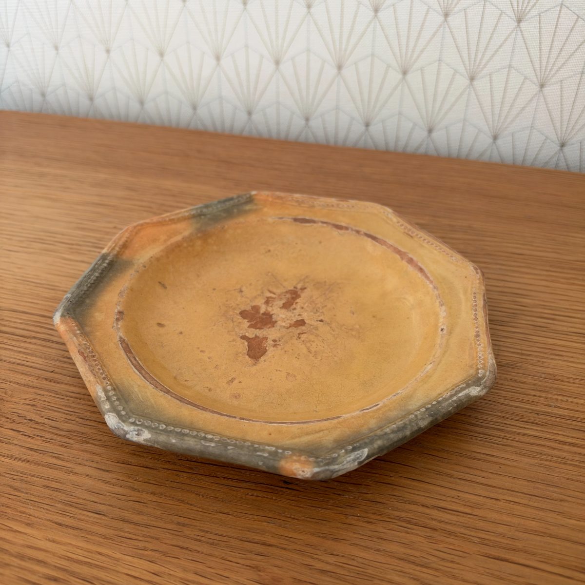 Overhead view of antique French octagonal earthenware plate with ochre yellow glaze and unglazed grey edges.