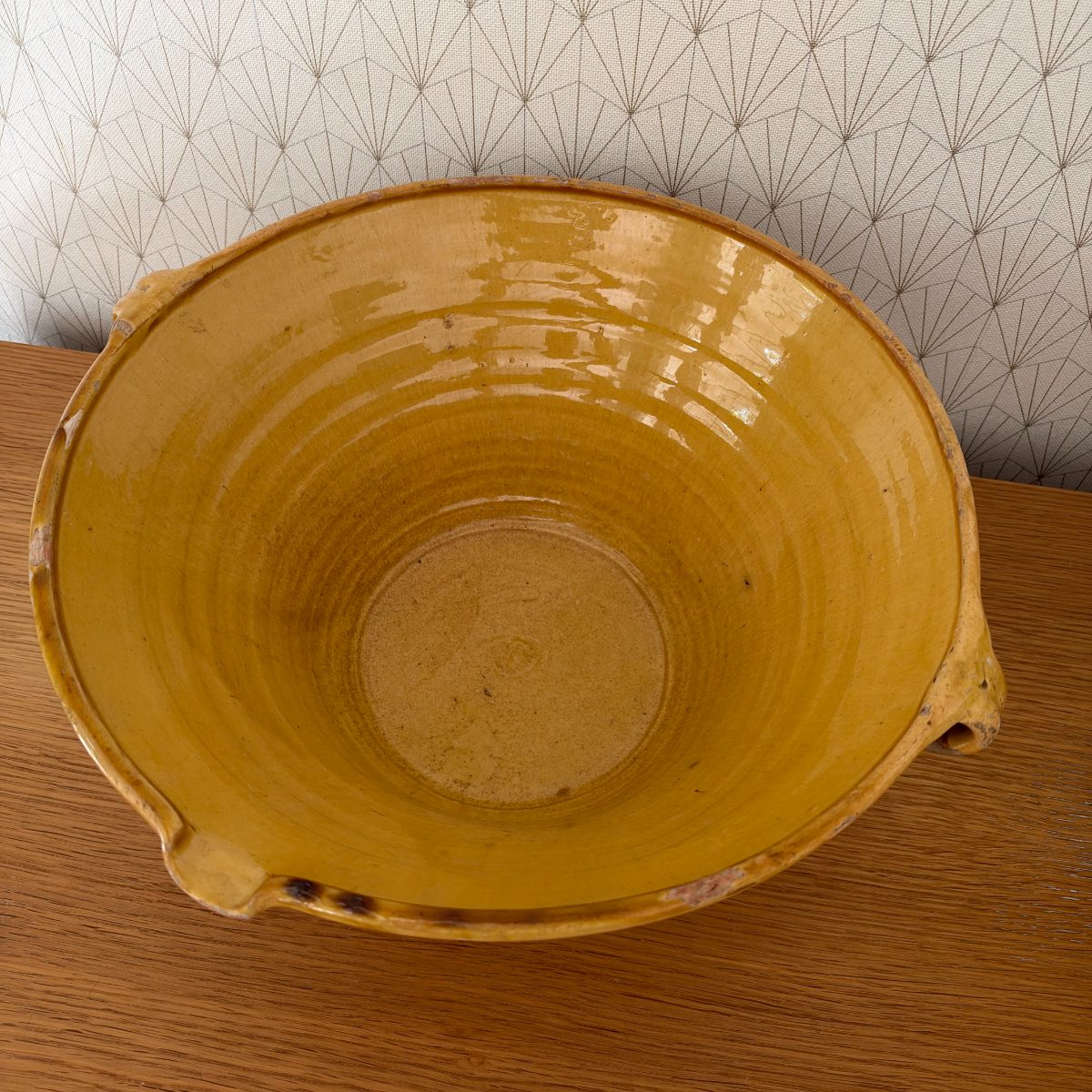 Top-down view of antique French terracotta tian bowl showing full ochre glazed interior, concentric throwing lines, unglazed center foot, and two loop handles.