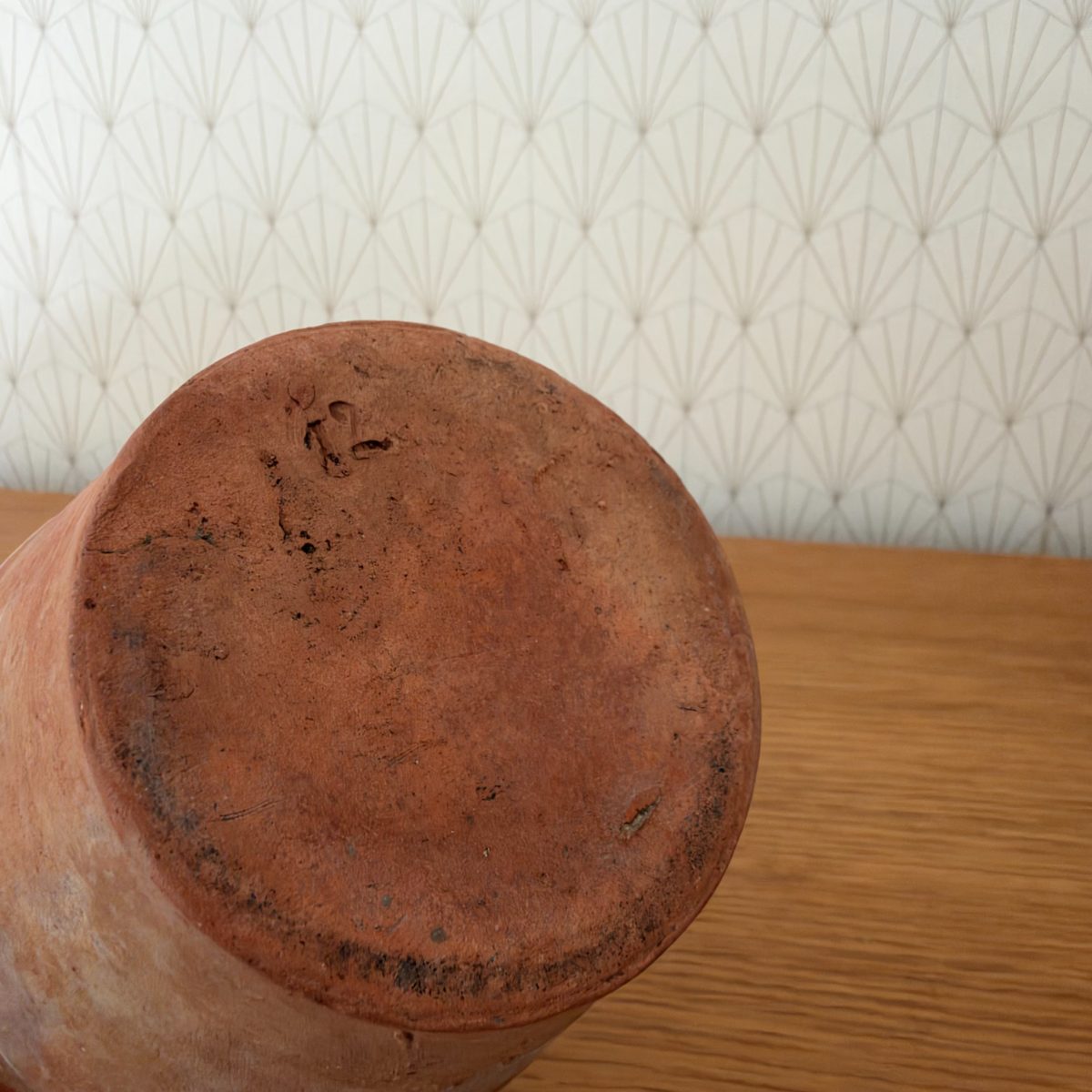 Bottom of antique French earthenware pot showing unglazed terracotta foot with impressed mark, age grime and natural clay texture.