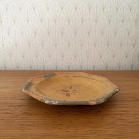 Antique French octagonal earthenware plate with amber yellow glaze and grey rim, side view on oak table.
