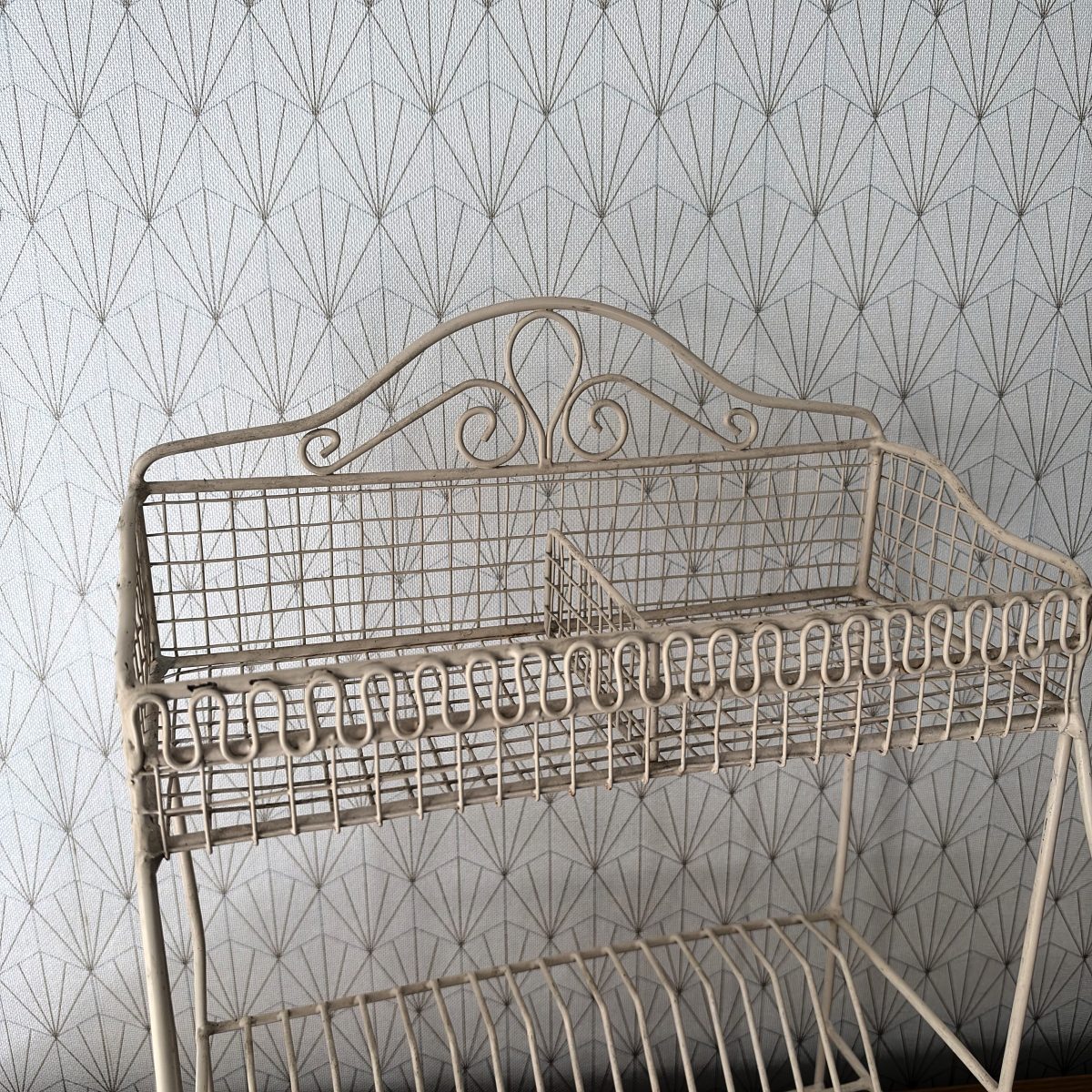 Close-up of the upper basket of a French white wire egouttoir showing ornate scrolled crest and looped wire decorative border along the front.