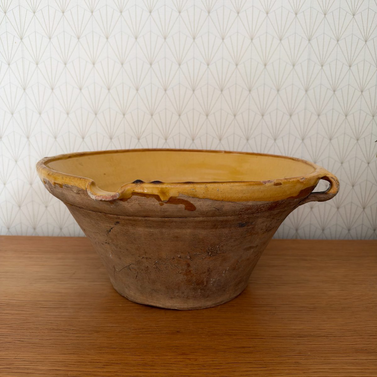 Antique French terracotta tian bowl with ochre yellow interior glaze and unglazed exterior, side view showing two small loop handles and glaze drips, on oak table.