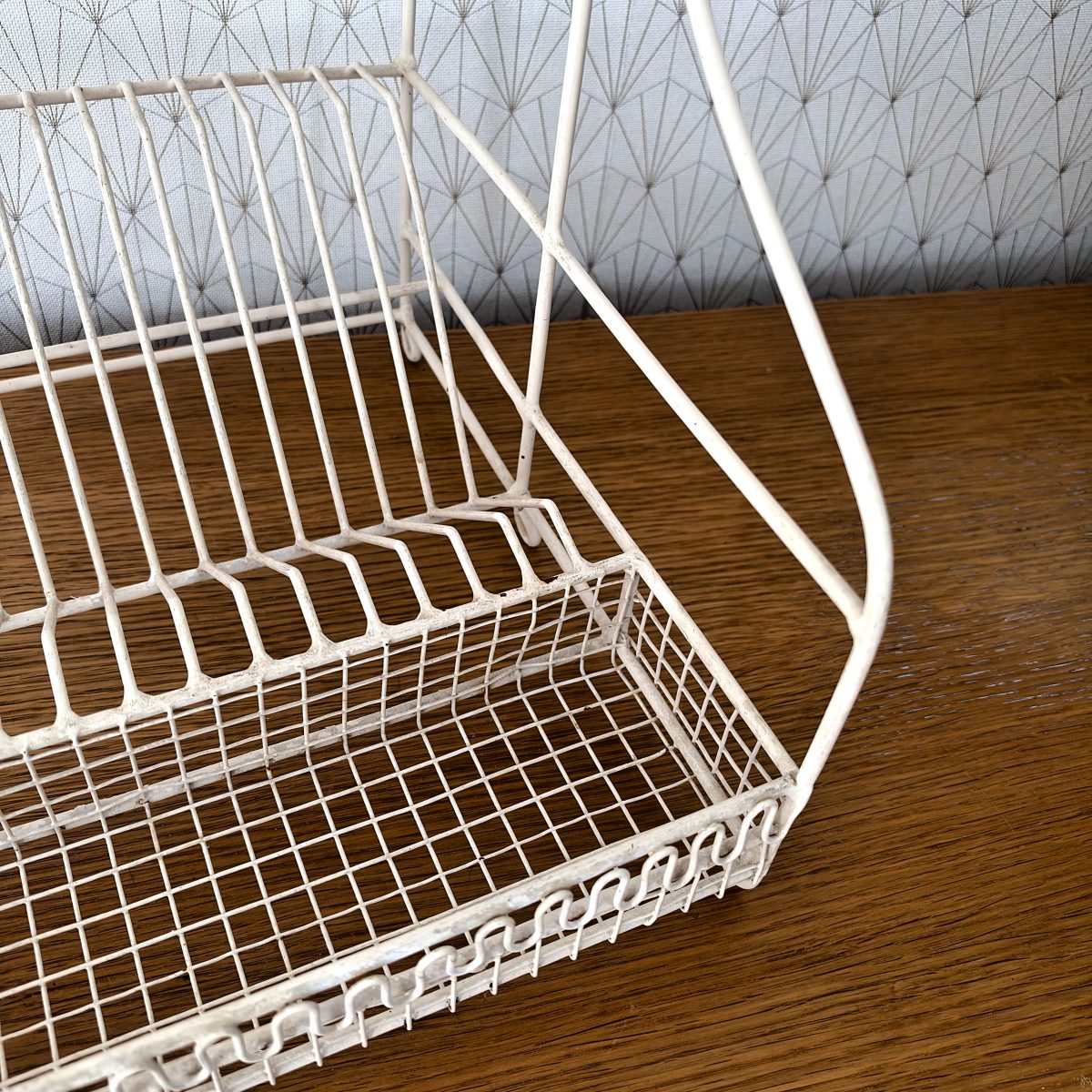Close-up of the lower drip tray basket of a French vintage white wire egouttoir showing fine mesh base and looped decorative wire trim.