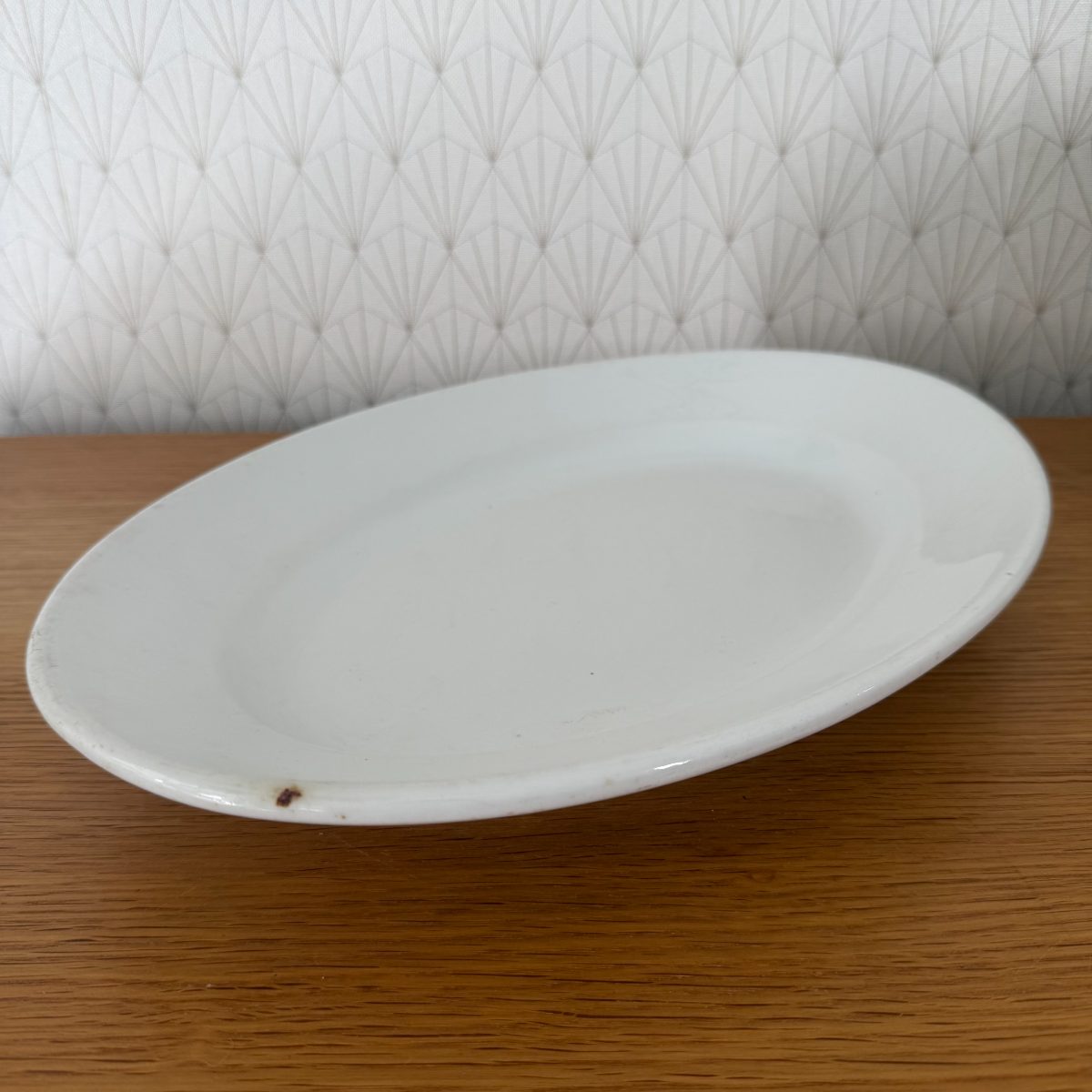 Three-quarter view of antique French white ironstone oval platter from opposite side showing glaze texture and small spot.