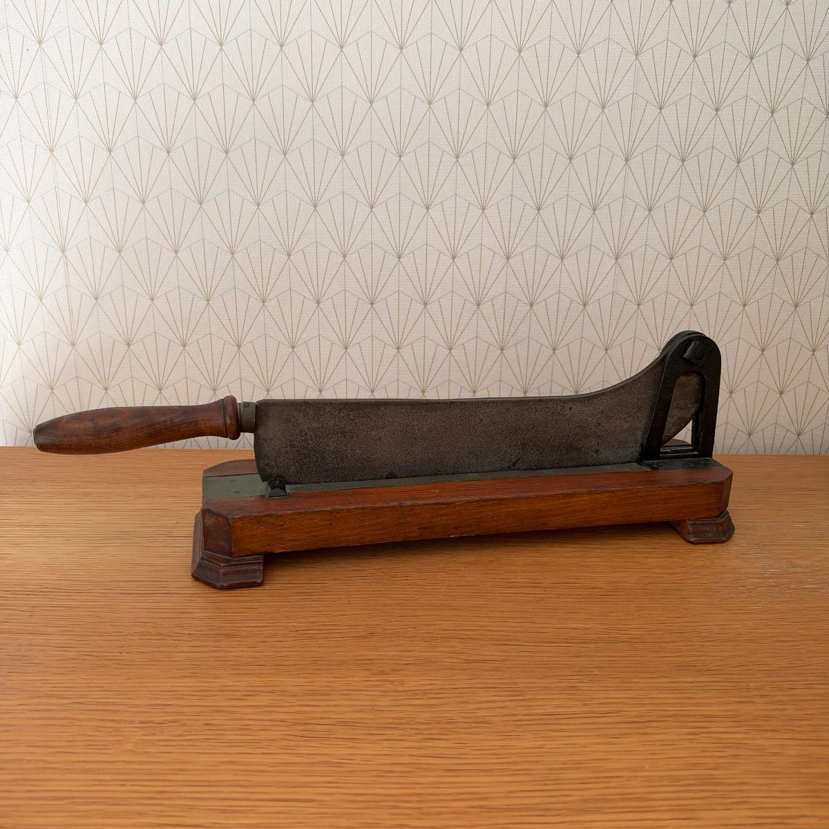 Antique French cast iron bread slicer full side view showing heavy iron blade body mounted on rectangular wood platform with small feet.