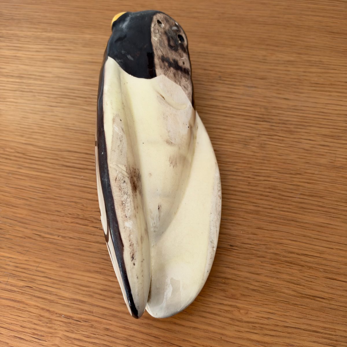 Underside of French ceramic cicada figurine showing unglazed cream base with visible wear and small holes, natural aging visible.