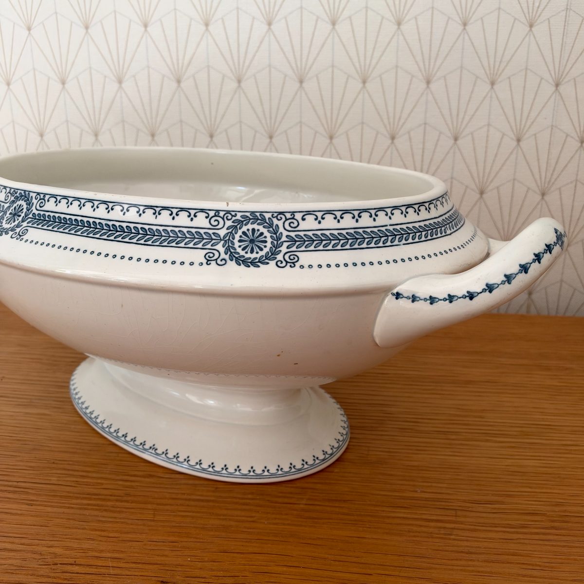 Side close-up of antique French ironstone tureen base showing neoclassical blue transferware band with rosette medallions, scrolls, and laurel motifs.