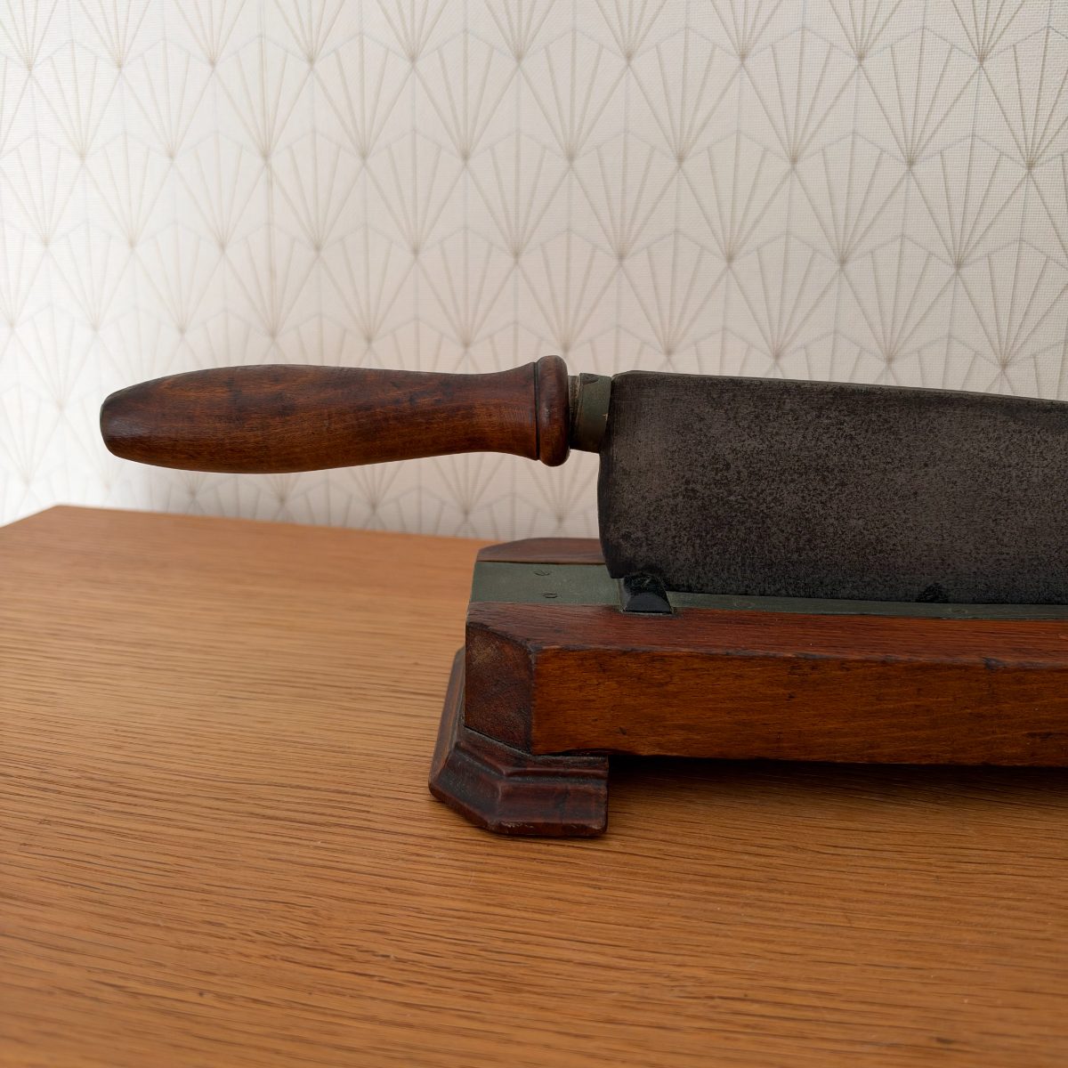 Handle end close-up of antique French cast iron bread slicer showing turned dark wood handle attached to heavy iron blade body.