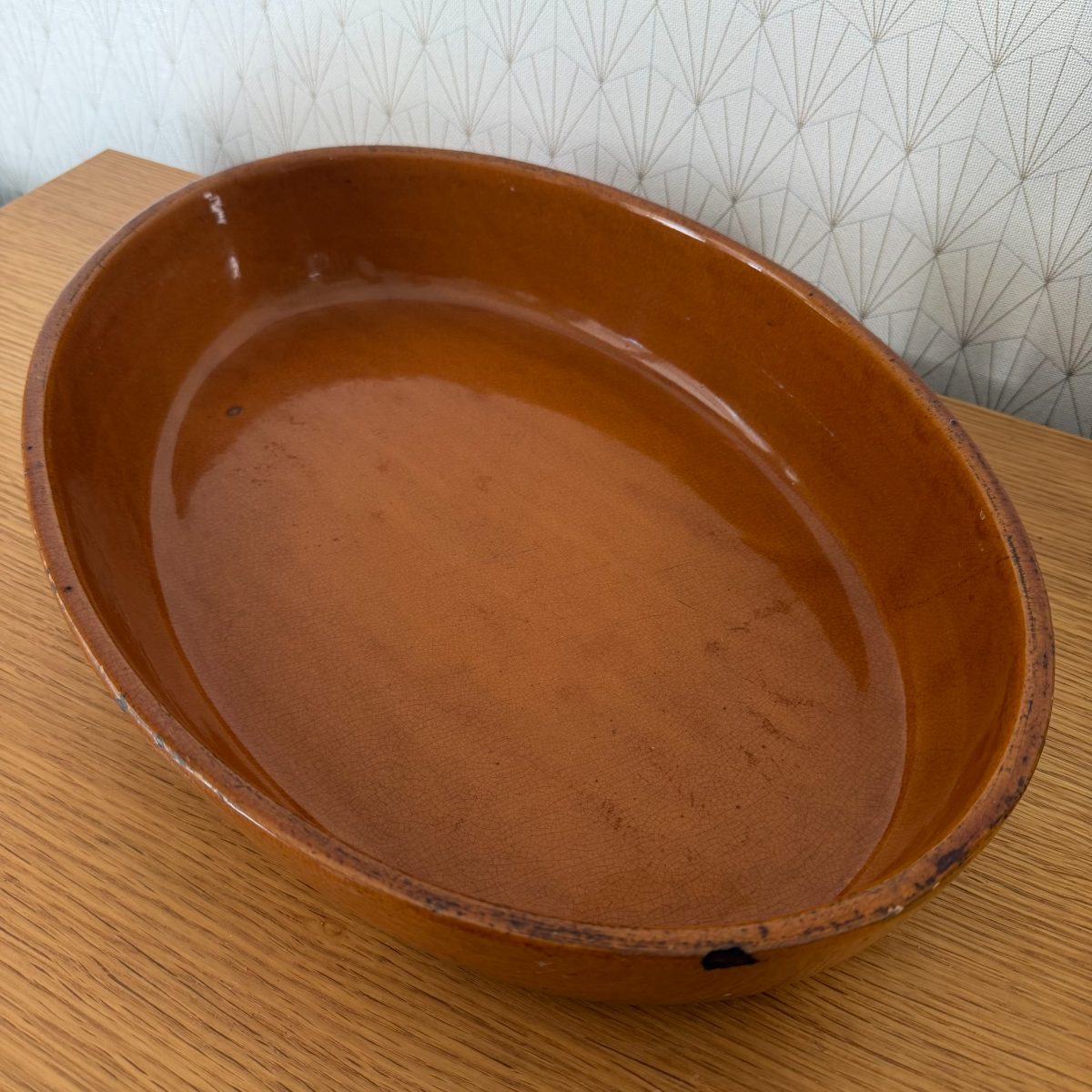 Bird's eye view into French terracotta oval dish interior revealing warm amber glaze and shallow depth of the vessel.