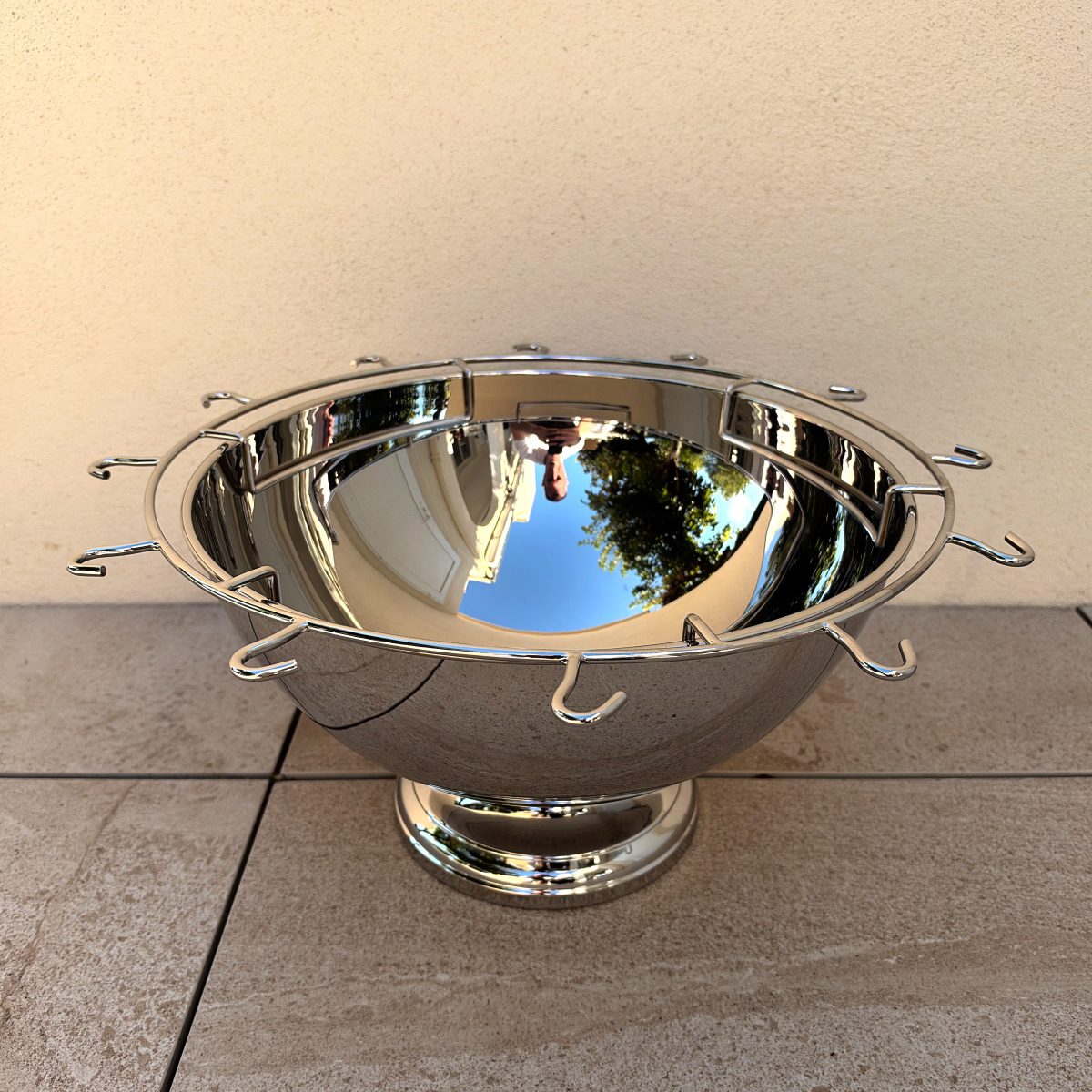 Guy Degrenne stainless champagne punch bowl seen from the front at slight elevation, showing the full ring of J-hooks for holding flutes.