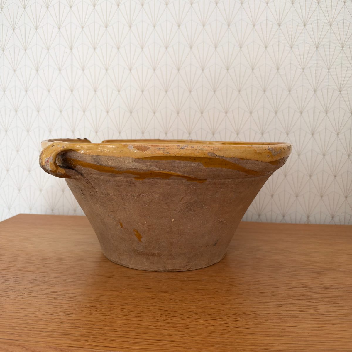 Close side view of antique French terracotta tian bowl showing one loop handle with ochre glaze drip running down the unglazed exterior wall.