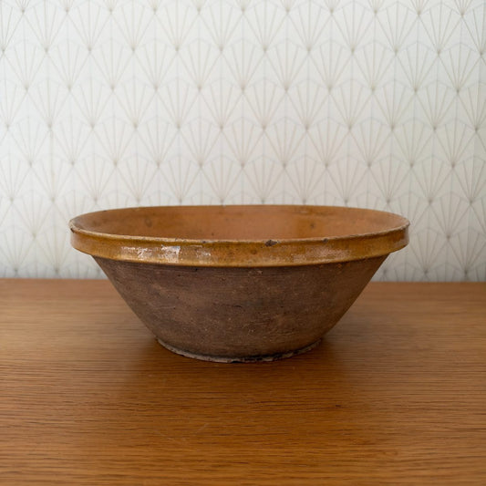 Antique French terracotta tian bowl with amber glaze interior and unglazed exterior, side view on oak table.