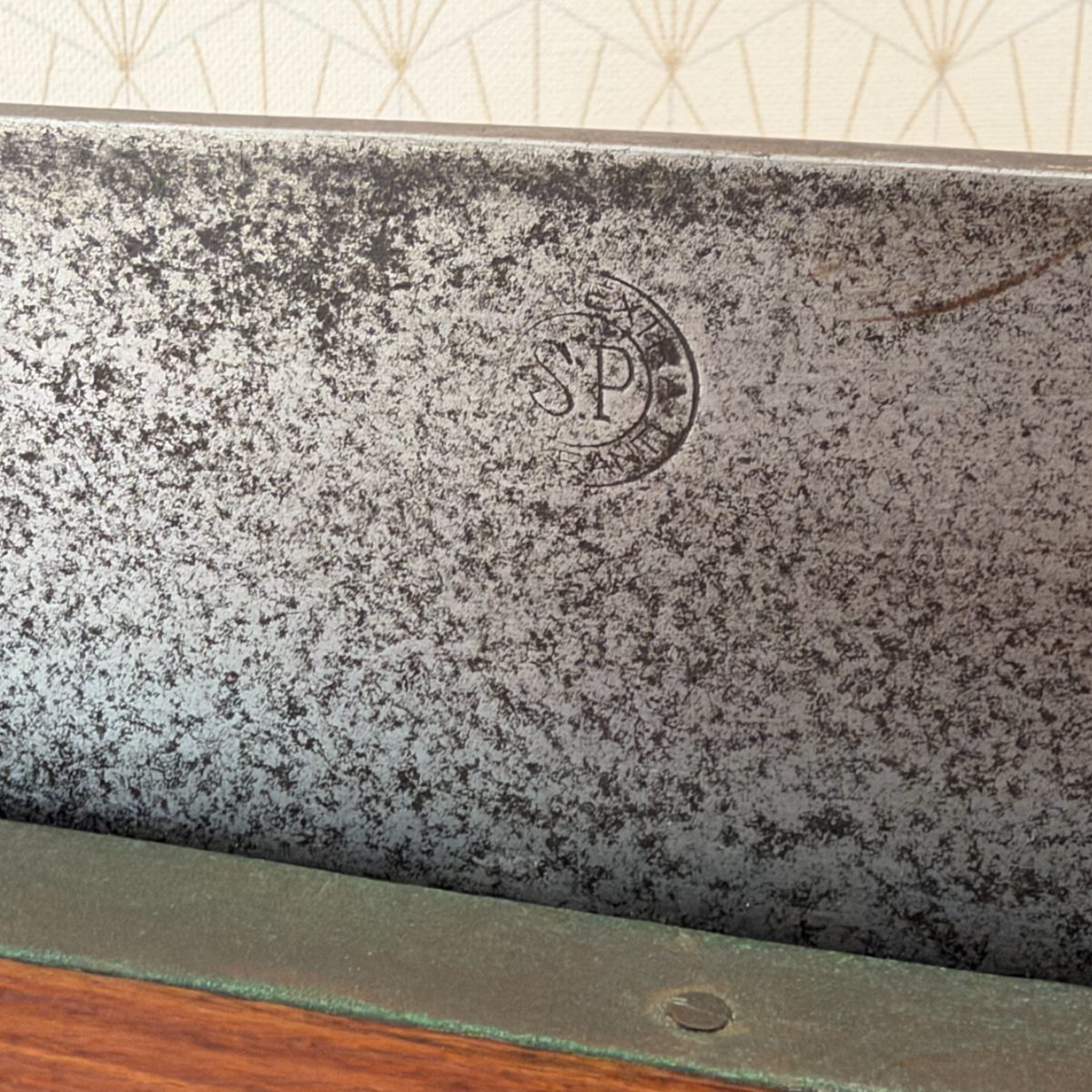 Close-up of cast iron blade surface of antique French bread slicer showing oval maker stamp with initials SP and partial surrounding text.