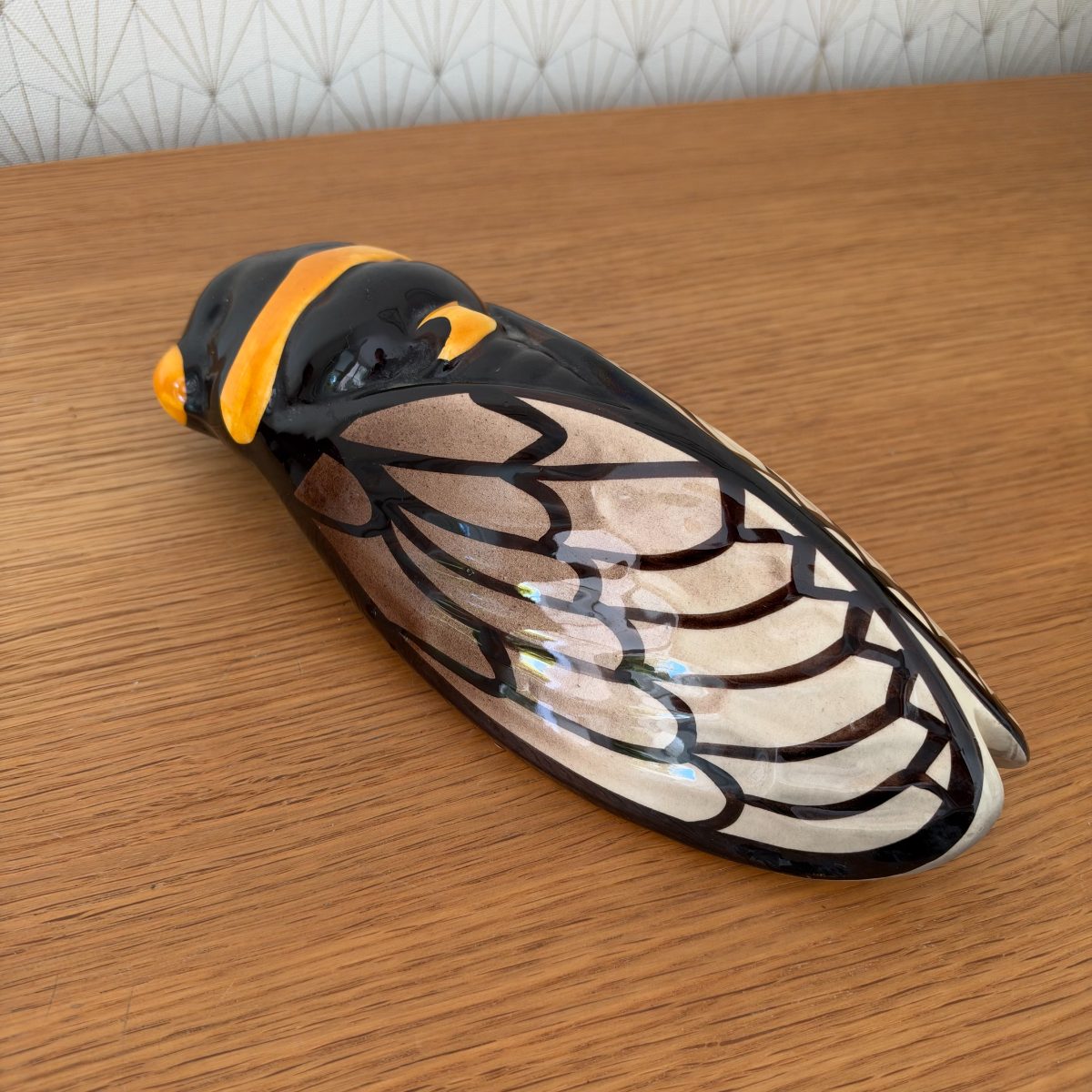 Three-quarter view of French painted ceramic cicada figurine showing glossy black body with amber stripe and translucent wing pattern.