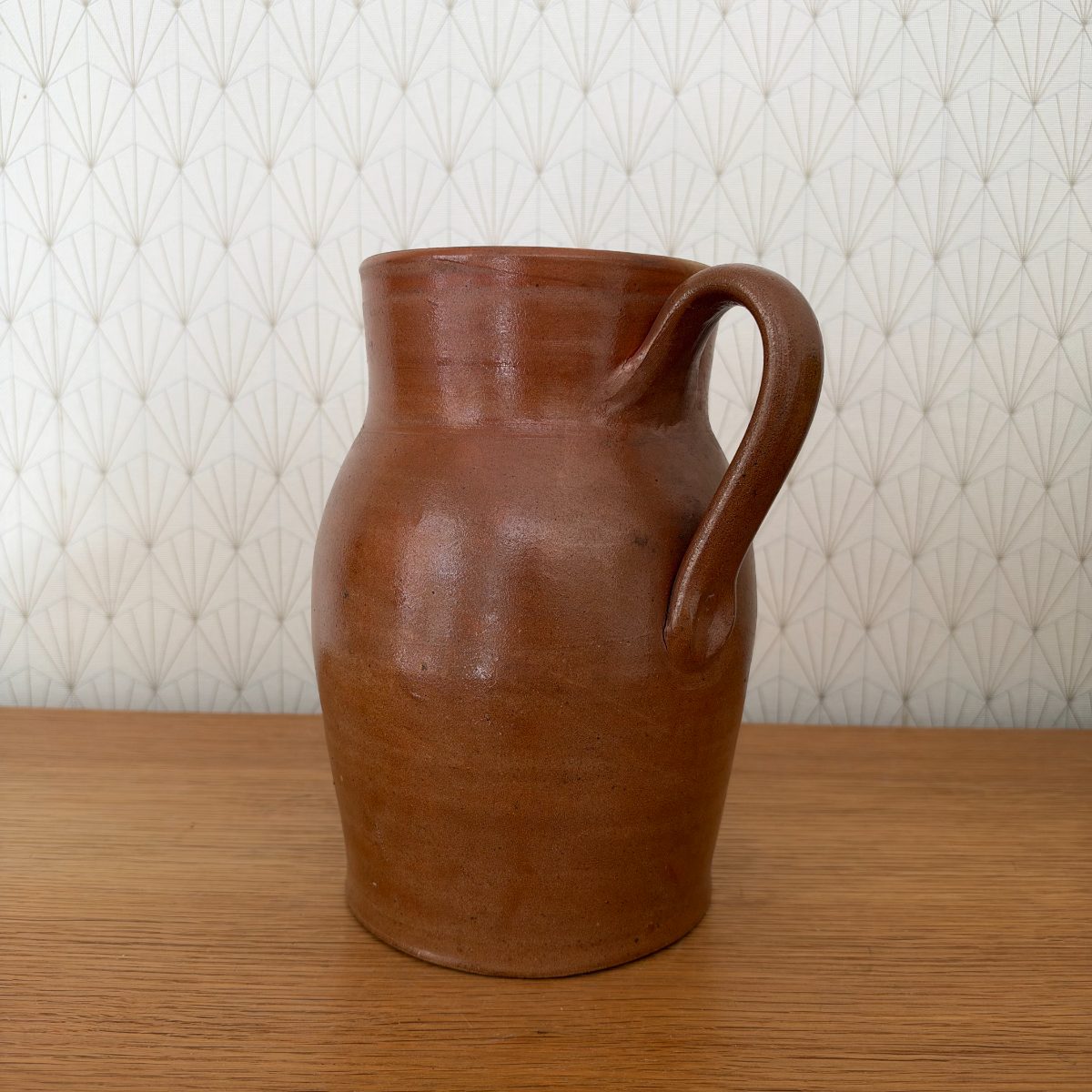 Rear view of antique French brown stoneware pitcher showing handle attachment and matte lower body.
