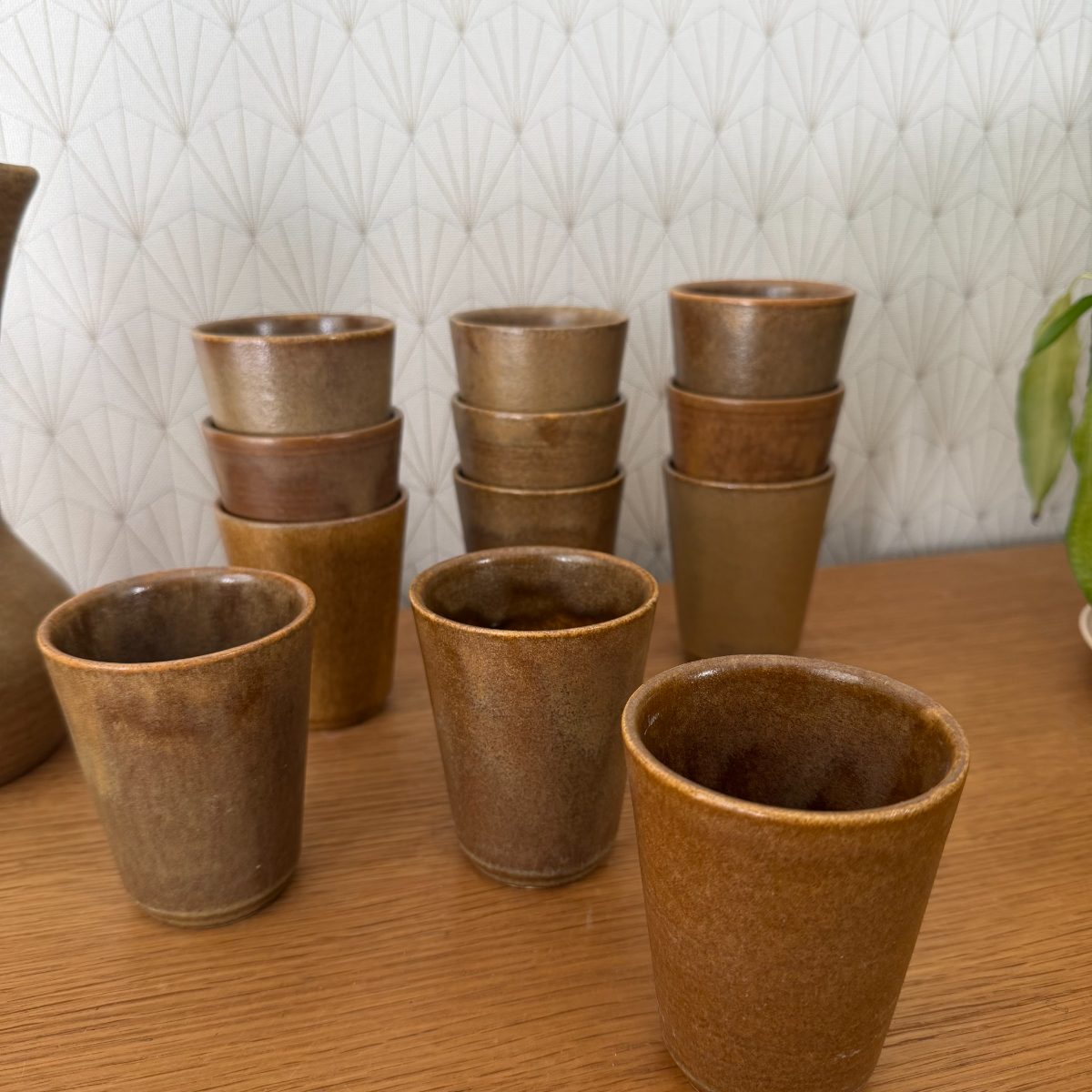 Twelve French stoneware cups in graduated amber and brown glazes arranged in stacks of three on a wood table