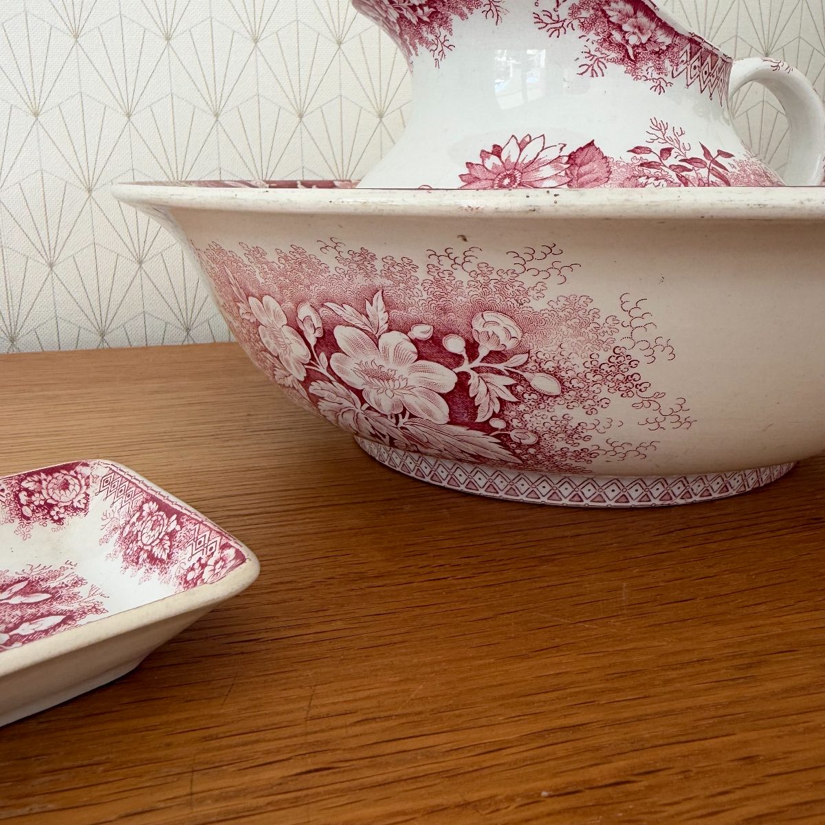 Side view of red transferware ironstone wash basin showing exterior floral decoration and diamond band border, with soap dish in foreground.