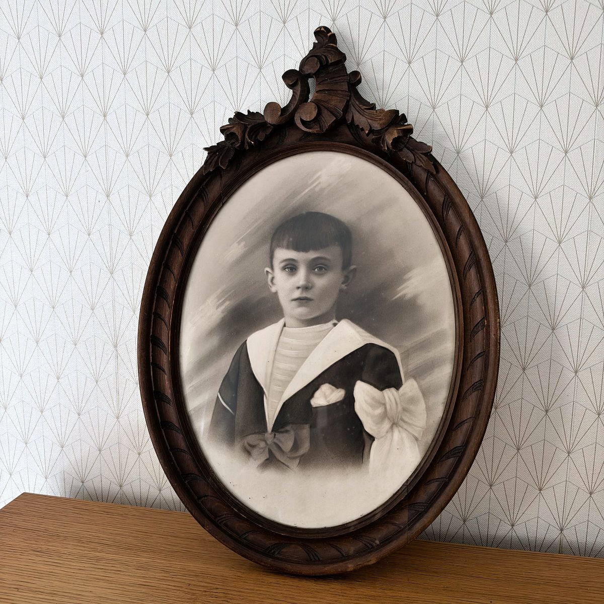 Full view of antique French oval carved frame with sepia boy portrait, ornate carved crest, rope-twist border detail, standing on wooden surface.